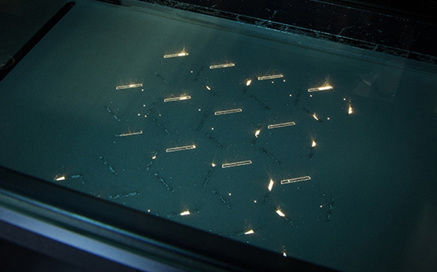 Metal powder is brushed away from a bed of intricate aluminum parts