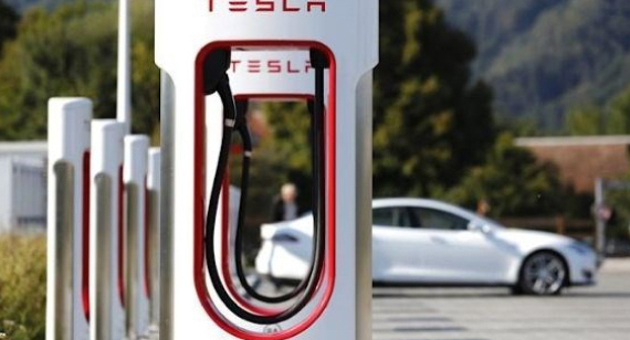 A tesla EV charging station with a white tesla car charging in the distance