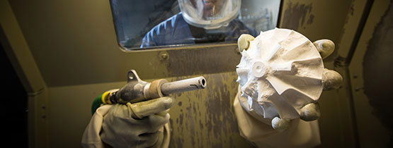 Gloved hands sandblasting a white 3D-printed object