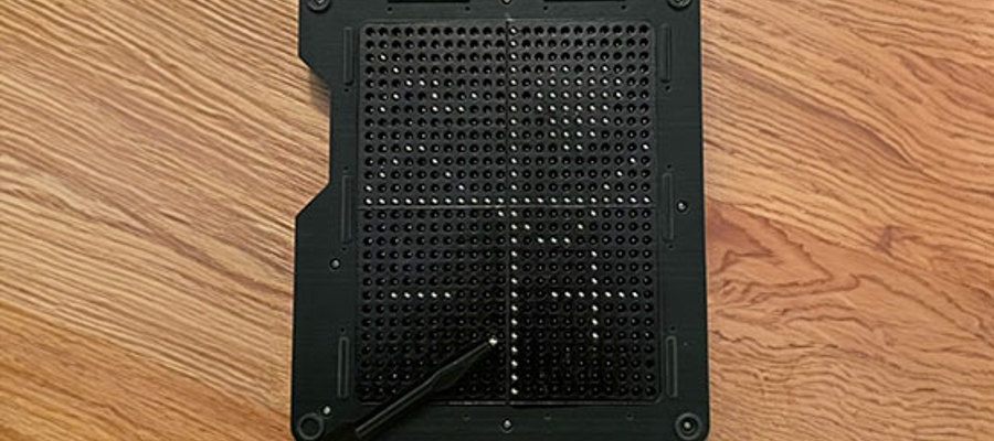 Black tactile board with grid pattern and stylus on a wooden surface.