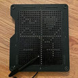 Black tactile board with grid pattern and stylus on a wooden surface.